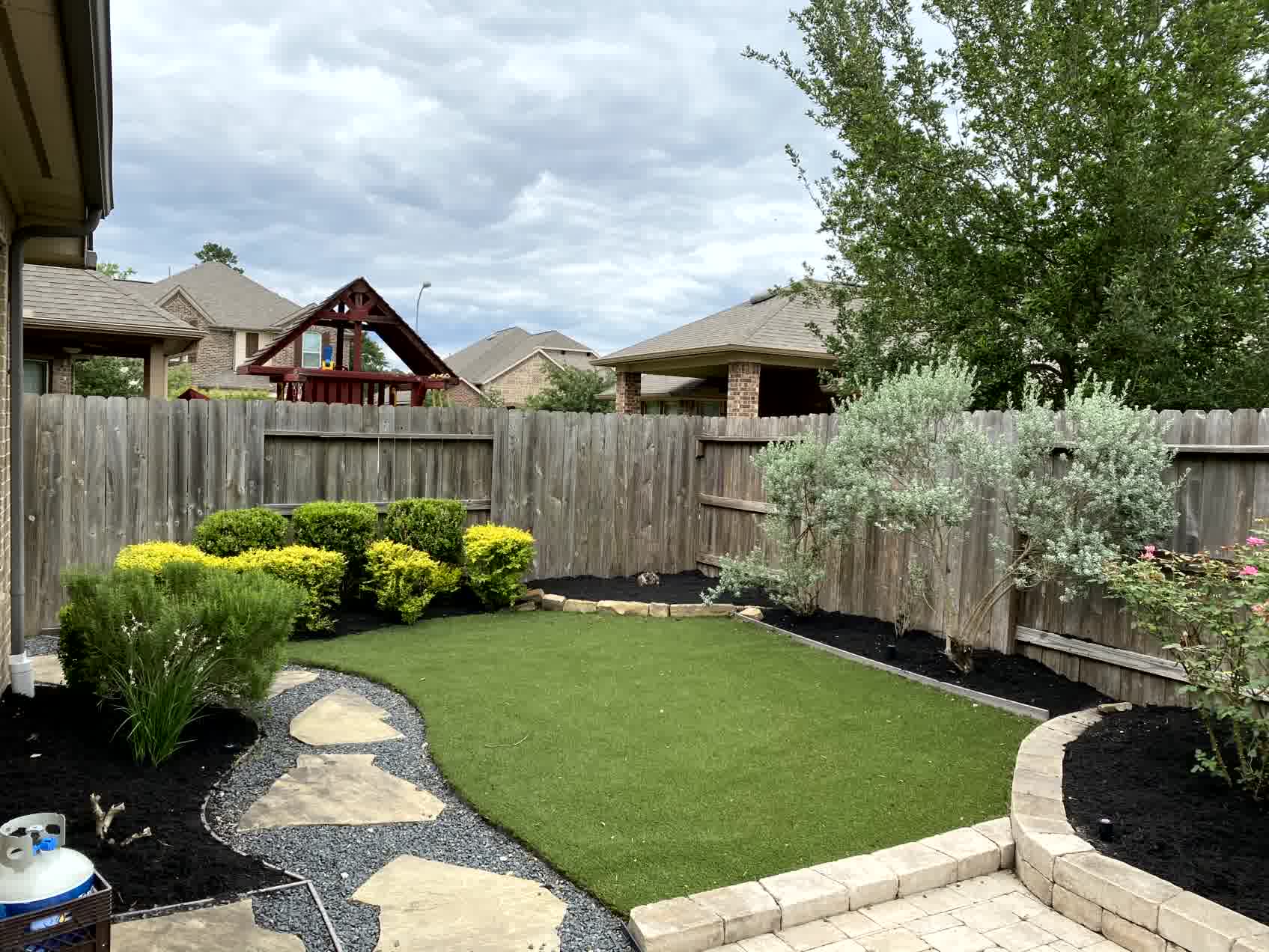 cut n edge the woodlands sod lawn mowing -Cut'N Edge Property Management Close view of backyard sod installation with flagstone walkway, bright yellow shrubs, and clean mulch beds along wood fencing.